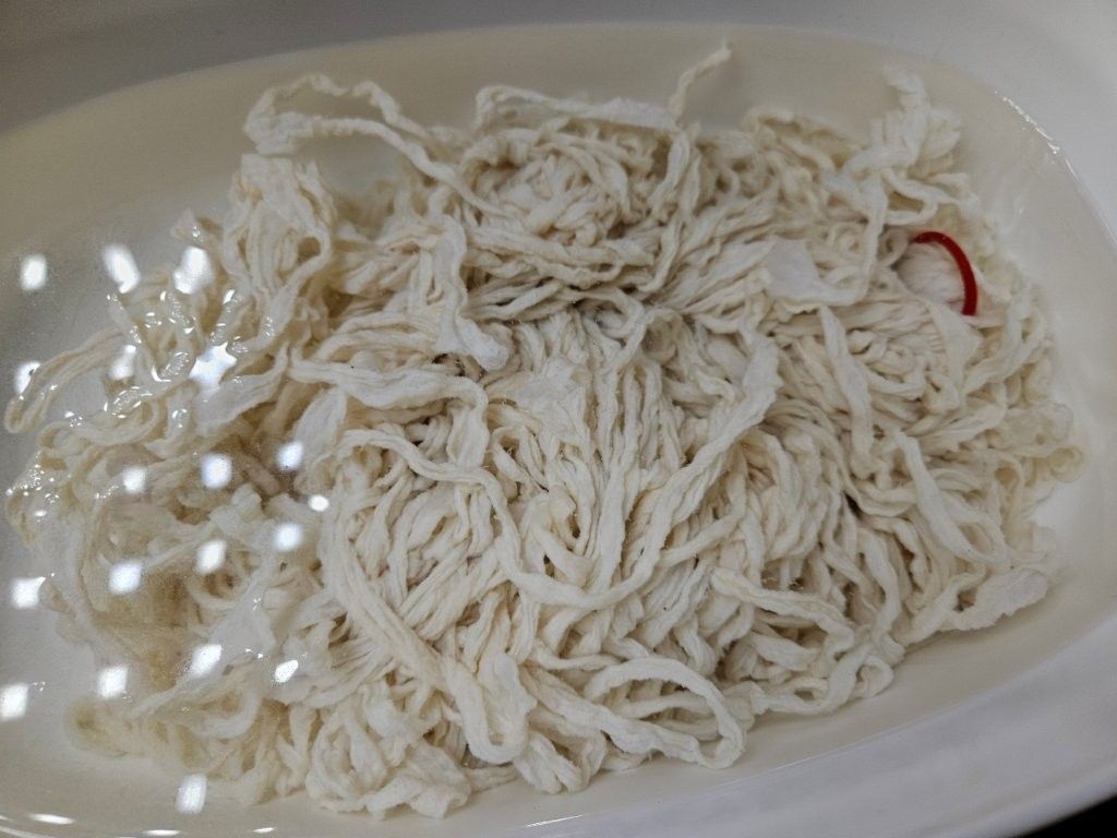 Weiße Innereien in einer weißen Schüssel, möglicherweise Kutteln, mit einigen roten Speiseresten.
