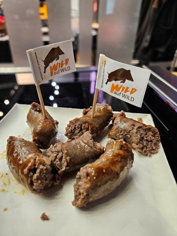 Würstchenhappen auf einem Teller, beschriftet mit „Wild & Wild“. Jeder Happen hat einen Zahnstocherfähnchen.