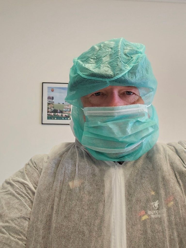 Person in vollständiger Schutzausrüstung, einschließlich Maske, Kappe und Overall, in einem Innenraum.