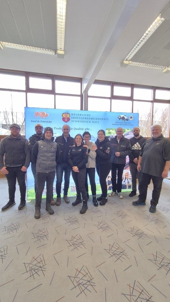 Eine Gruppe von Menschen posiert vor einem Banner. Sonnenlicht fällt durch die Fenster.