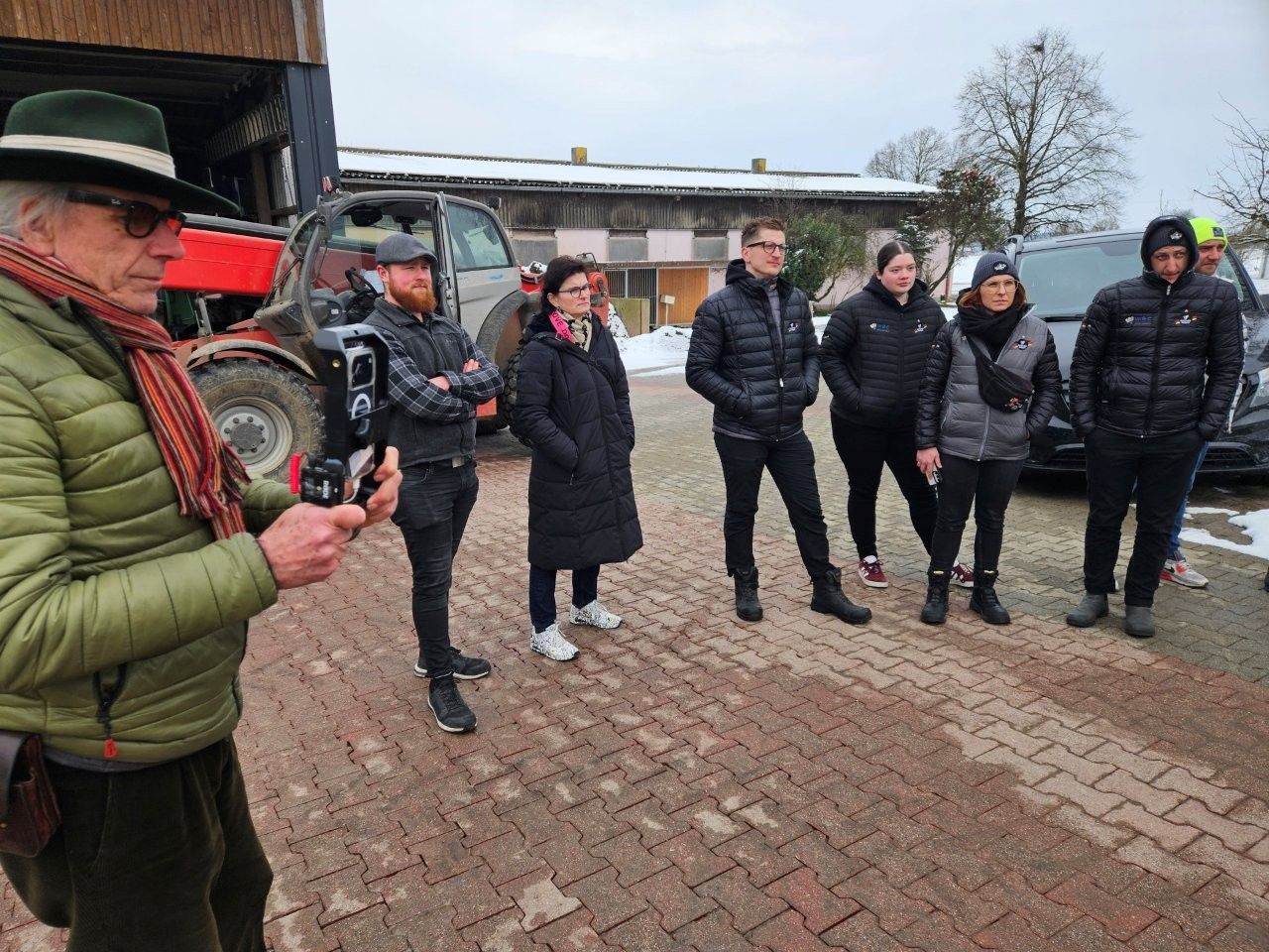 Eine Gruppe von Menschen steht vor einem Gebäude. Ein Mann hält eine Kamera. Kalte, verschneite Umge