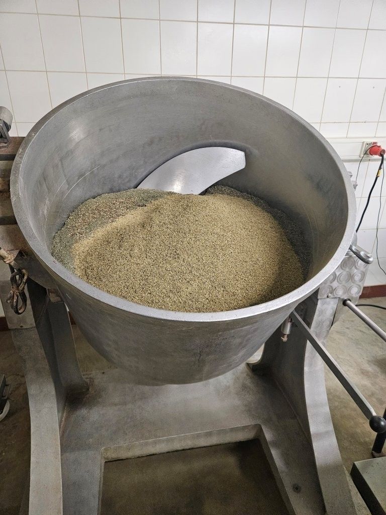 Großer industrieller Mischbehälter aus Edelstahl, gefüllt mit grünem Granulat, mit einem abgewinkelten Rührflügel.