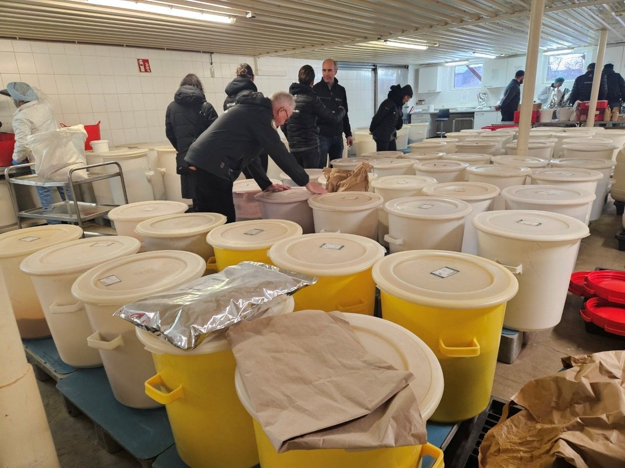 Menschen inspizieren zahlreiche weiße und gelbe Container in einem Lagerhaus. Einige Container sind geöffnet.