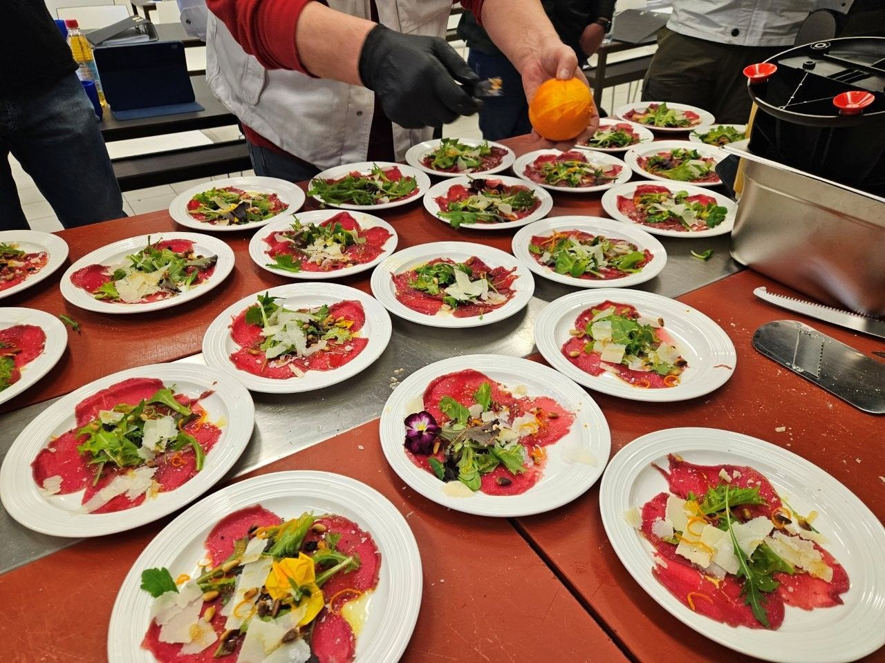 Ein Koch bereitet Teller mit Carpaccio, Rucola, Parmesan und essbaren Blüten zu.