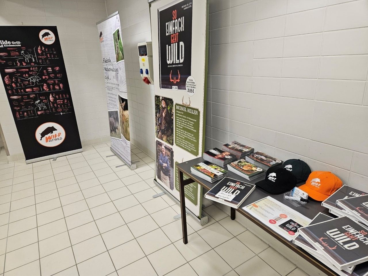Innenbereich mit Bannern, Büchern und Hüten auf einem Tisch. Plakate mit der Aufschrift „Into the Wild“.
