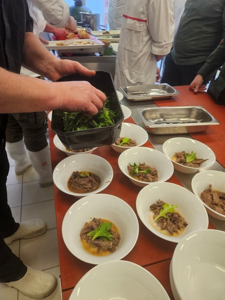 Ein Koch richtet in der Küche Gerichte mit Gemüse an. Mehrere gefüllte Schüsseln sind auf einer roten Fläche arrangiert.