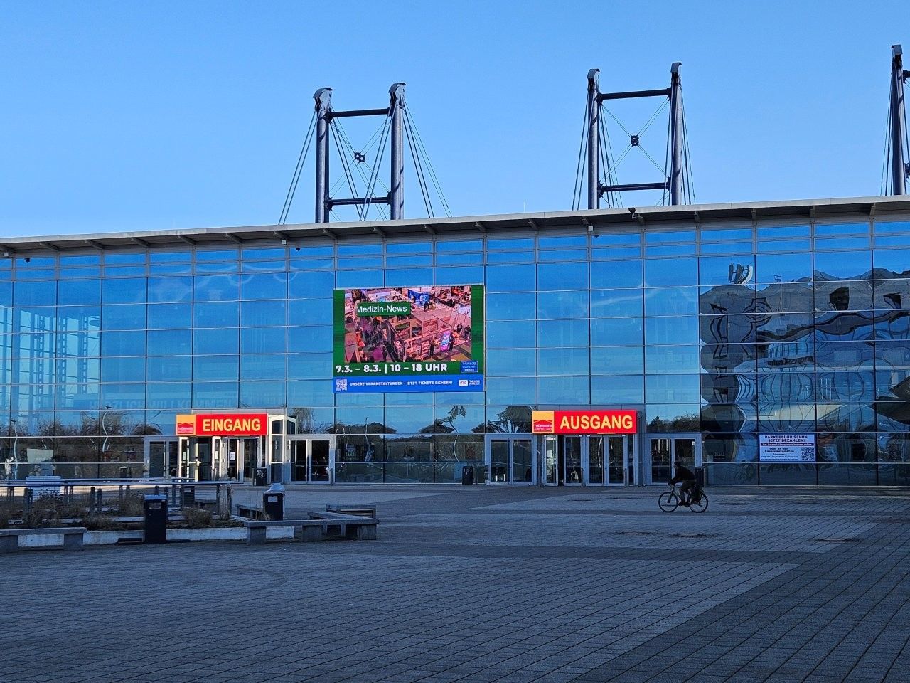 Außenansicht des Aarhus-Stadions mit großer blauer Glasfassade, Eingängen und einer Videoleinwand.