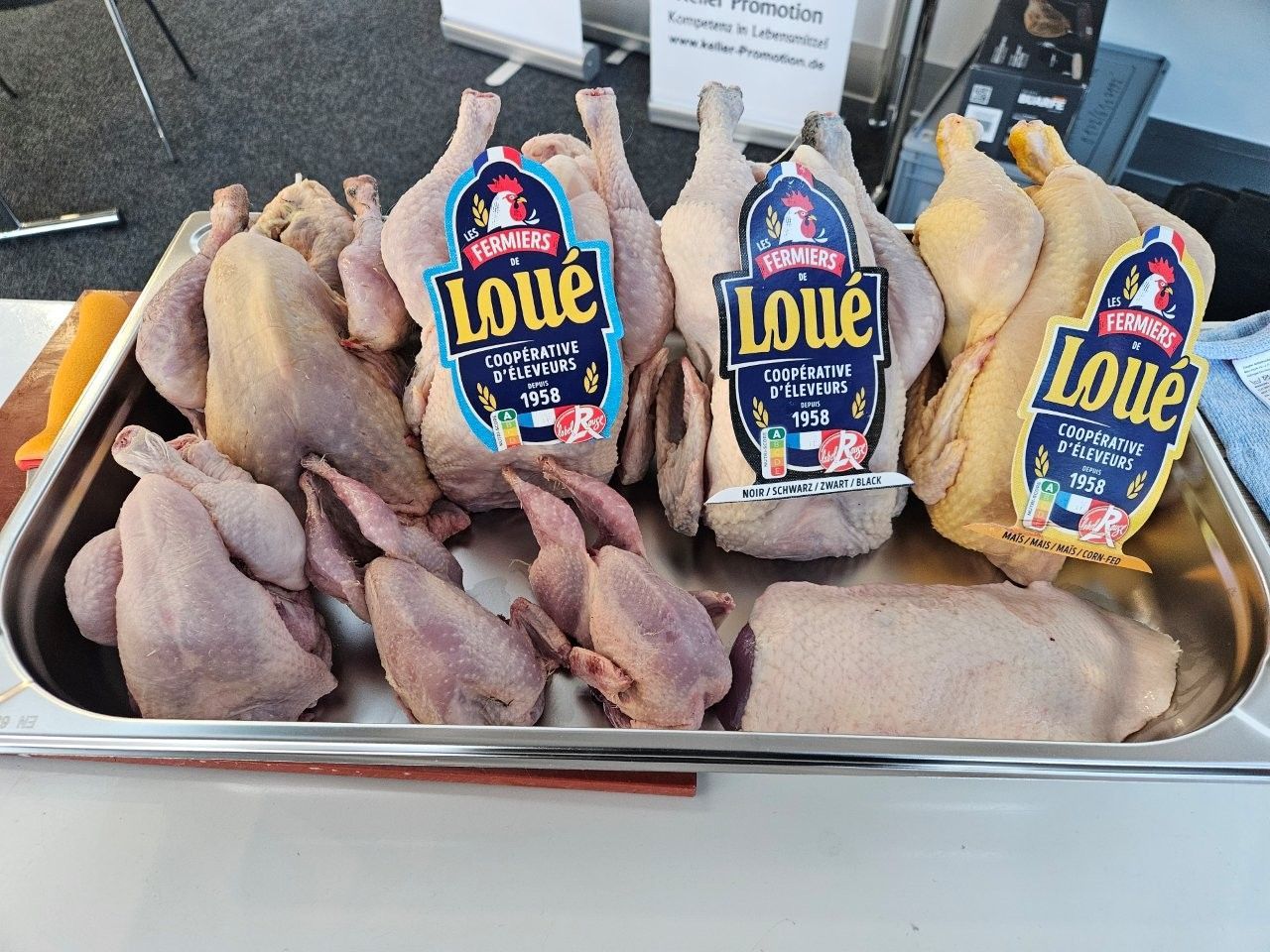 Rohes Geflügel mit der Aufschrift „Loué“ ist auf einem Metalltablett in einem Lebensmittelmarkt angerichtet.