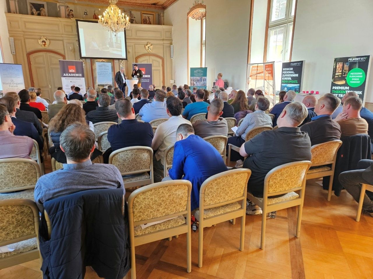 Das Publikum sitzt in einem holzgetäfelten Saal und blickt auf eine Podiumsdiskussion im vorderen Bereich.