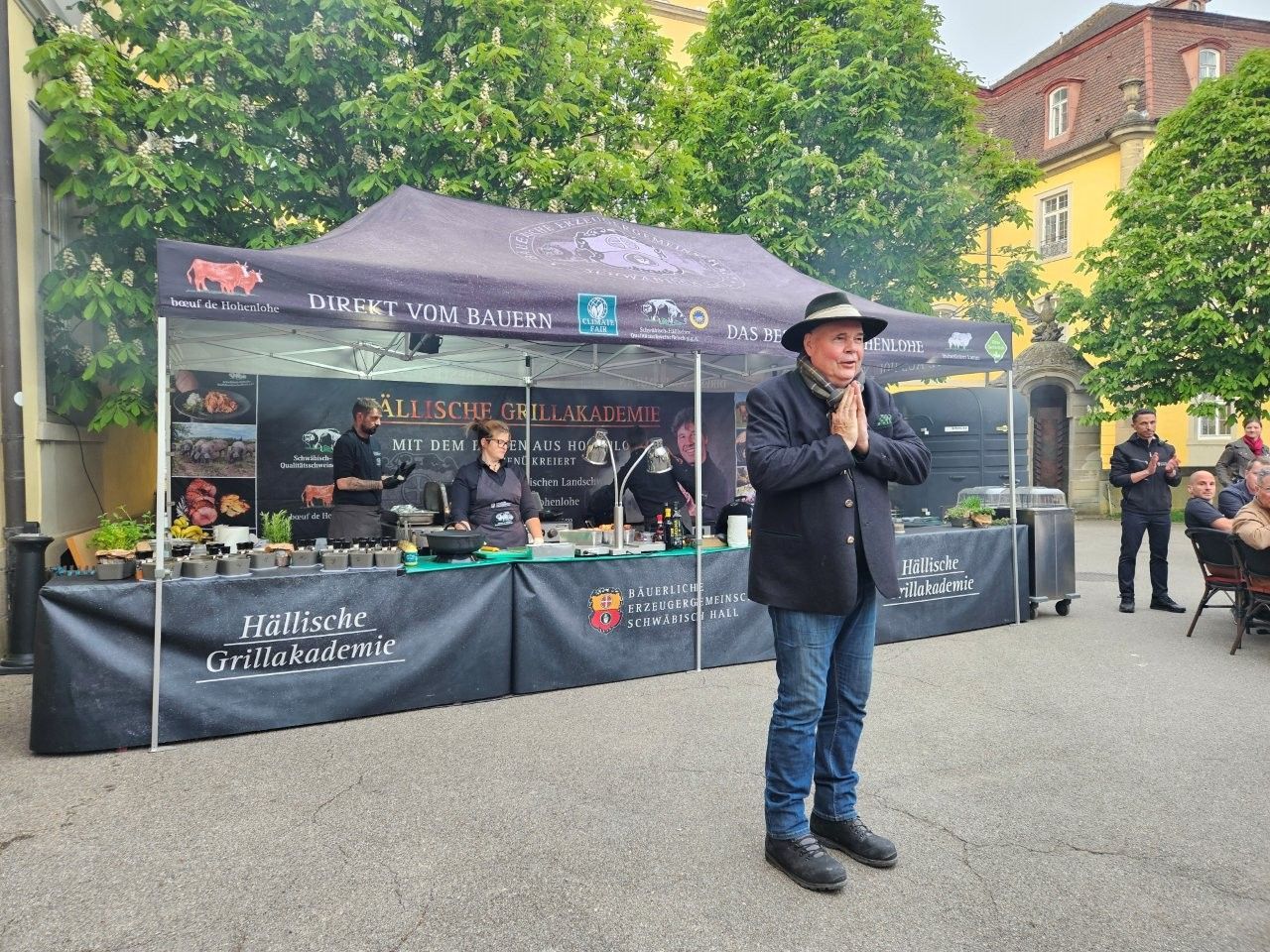 Marktstand an einer Straße, an dem ein Mann mit Hut im Freien in ein Mikrofon spricht