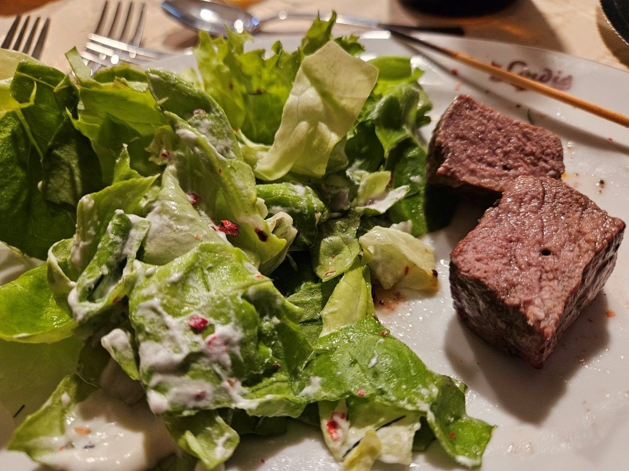 Ein Teller mit grünem Blattsalat und cremigem Dressing sowie zwei Steakstücke auf einem Esstisch