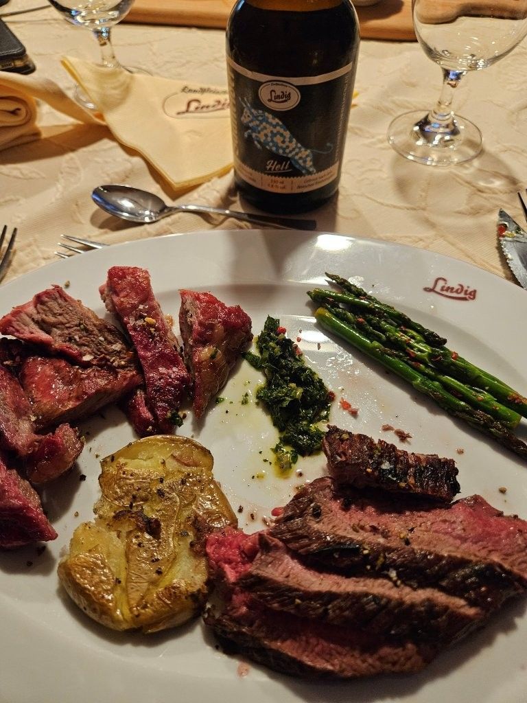 Ein Steak-Abendessen mit Bratkartoffeln, Spargel, Brot und einer Flasche Wein auf einem Tisch.