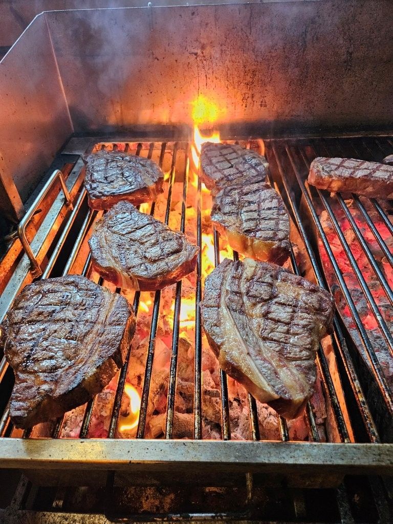 Steaks, die über offenem Feuer auf einem Grill zubereitet werden, mit Rauch und verkohlten Grillstreifen.