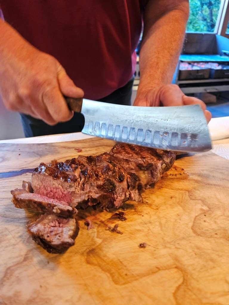 Eine Person schneidet ein gekochtes Steak mit einem großen Messer auf einem Holzbrett in Scheiben.