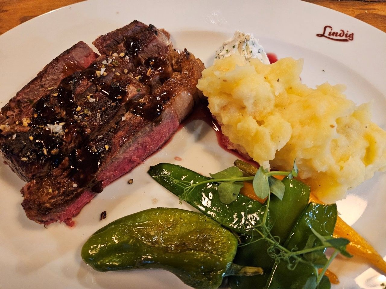 Gegrilltes Steak mit Kartoffelpüree und grünem Gemüse auf einem weißen Teller