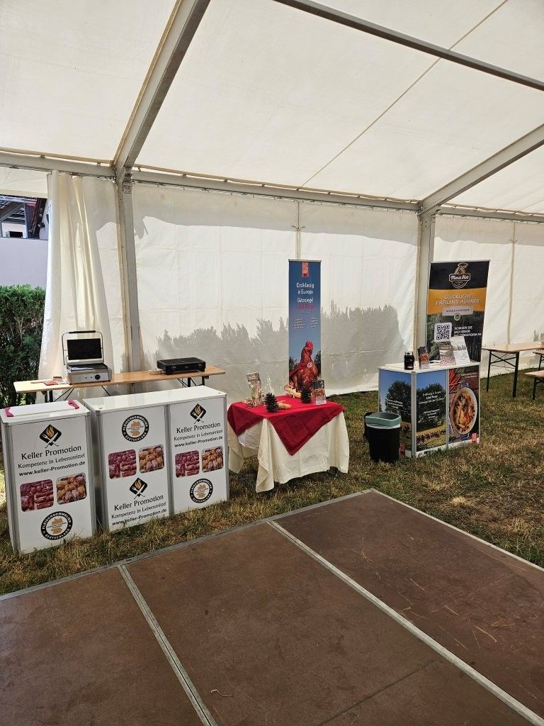 Messestand unter einem weißen Zelt mit Markenbehältern, Bannern und einem rot verhüllten Tisch.
