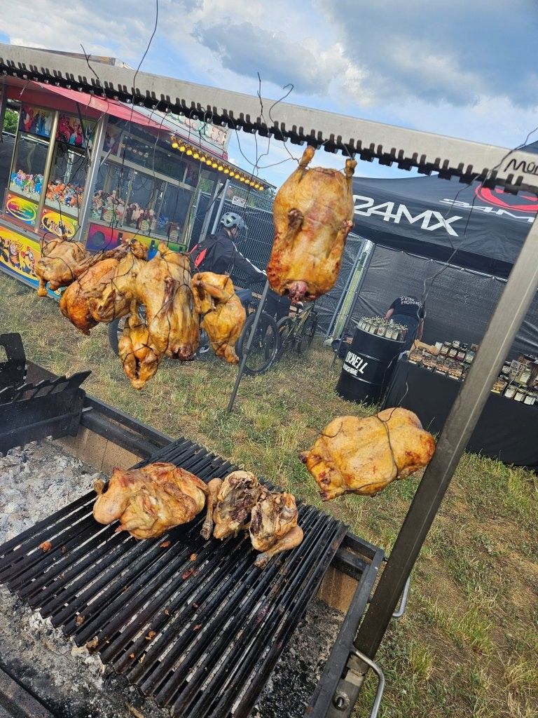 Grill mit mehreren gebräunten Hähnchen, die im Freien über Holzkohle auf einem Grillplatz garen