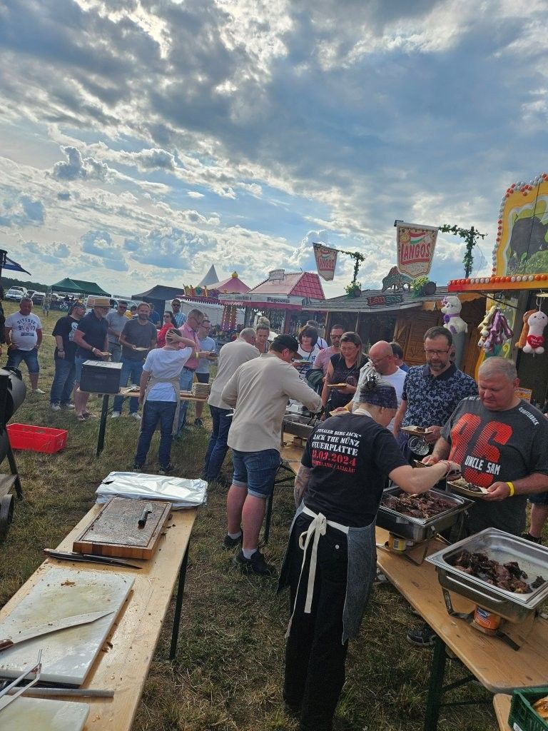 Menschen servieren Essen auf einem Freiluftfest mit Grills, Tischen und einem bewölkten Himmel