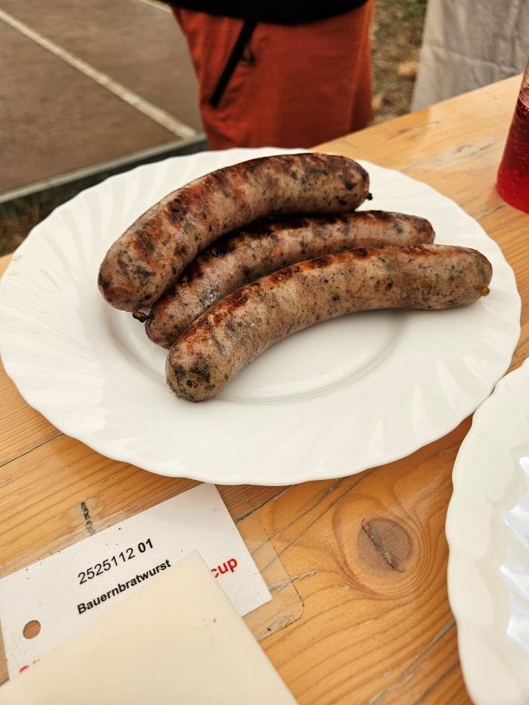 Drei gegrillte Würstchen auf einem weißen Teller auf einem Holztisch