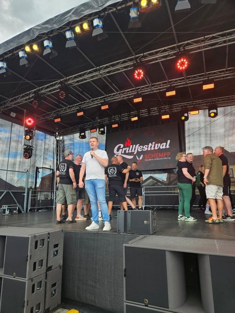 Open-Air-Musikfestivalbühne mit Künstlern und Crew unter rotem Licht und vor dem Hintergrund des „Glastfestival“.