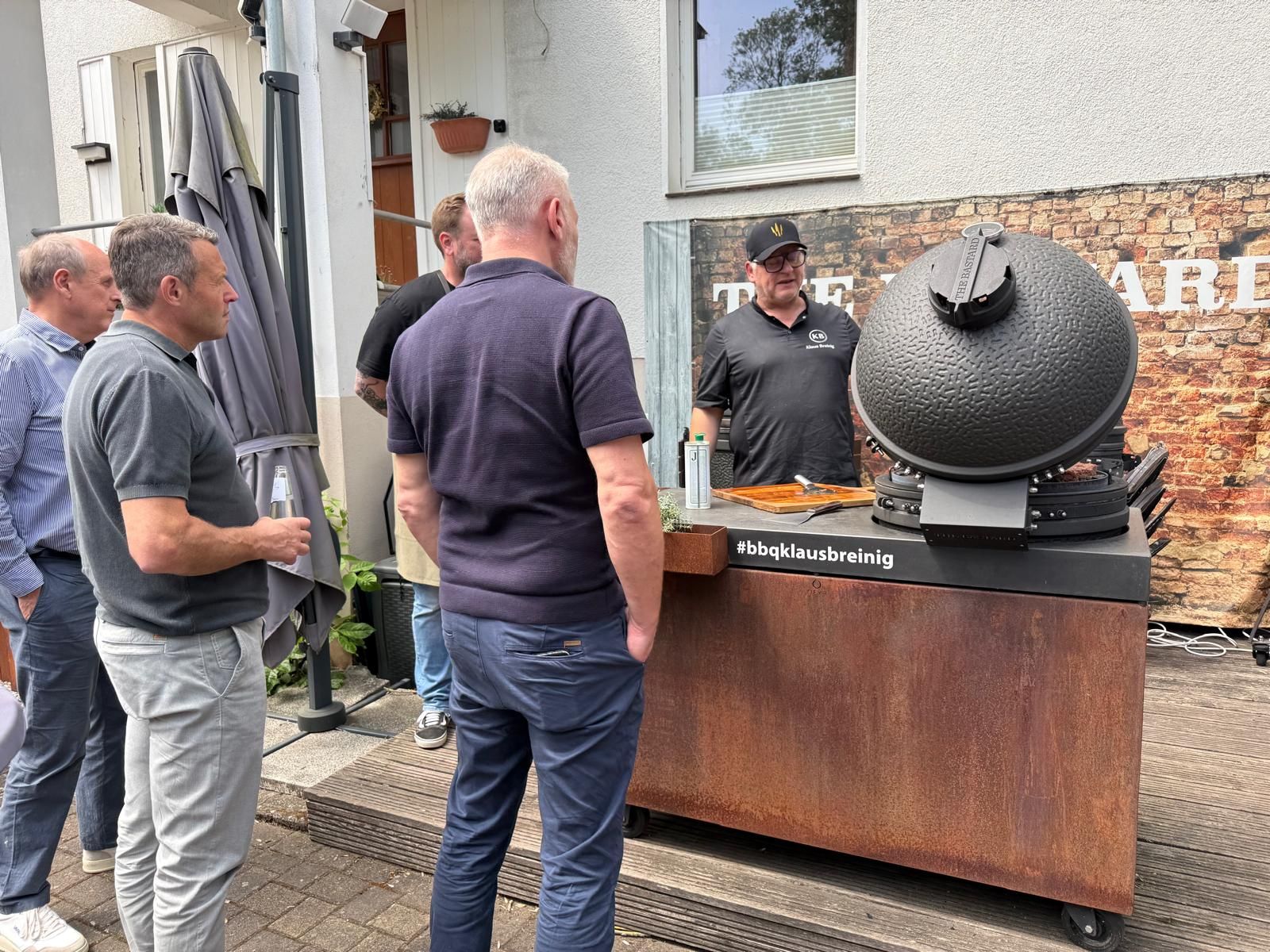 Männer versammelten sich im Freien neben einem Gebäude um einen großen schwarzen Metallgrill.