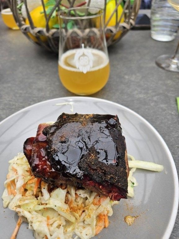 Gegrillte Rippchen auf Krautsalat mit Senf, dazu ein Glas Bier auf einem Tisch.