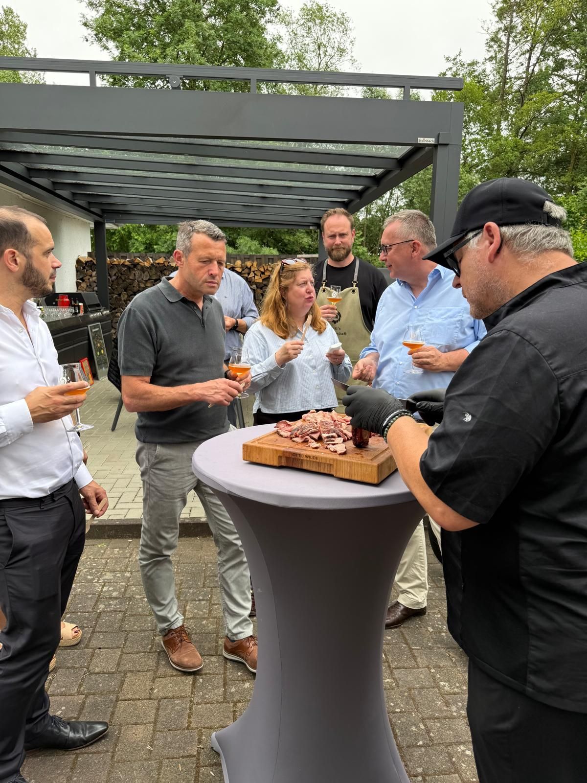 Die Menschen versammelten sich im Freien um einen hohen Tisch, tranken gemeinsam und schnitten eine Torte an.