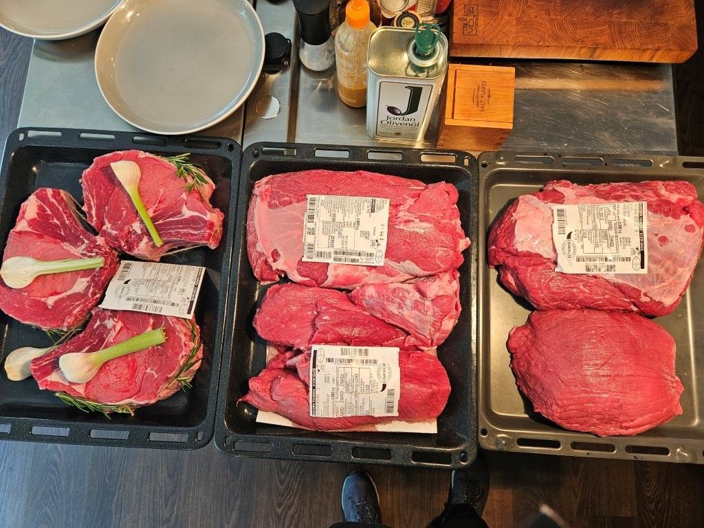 Verschiedene rohe Rindfleischstücke in Schaumstoffschalen mit Etiketten, auf einer Theke arrangiert.