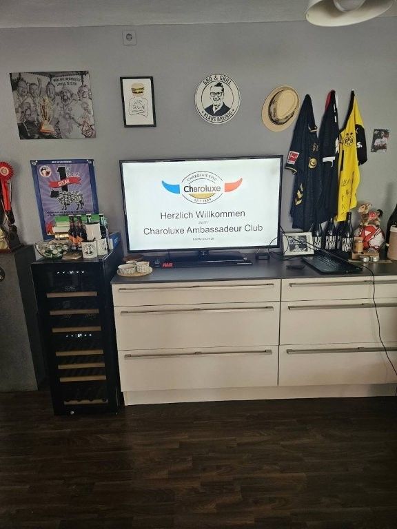 Wohnzimmerwand mit Fernseher, Kommode, gerahmten Bildern, Hüten und hängenden Sportuniformen