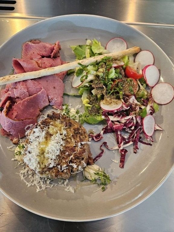 Teller mit in Scheiben geschnittenem Roastbeef, Salat, geriebenem Käse und Radieschenscheiben als Garnitur