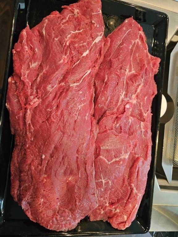 Rohe rote Fleischstücke auf einem schwarzen Tablett, von oben betrachtet.