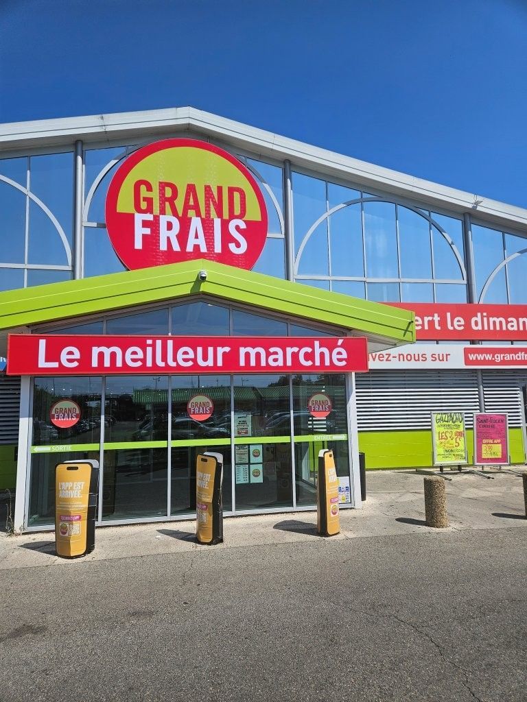 Eingang zum Grand Frais Supermarkt mit leuchtend roter Beschilderung und grüner Markise unter blauem Himmel