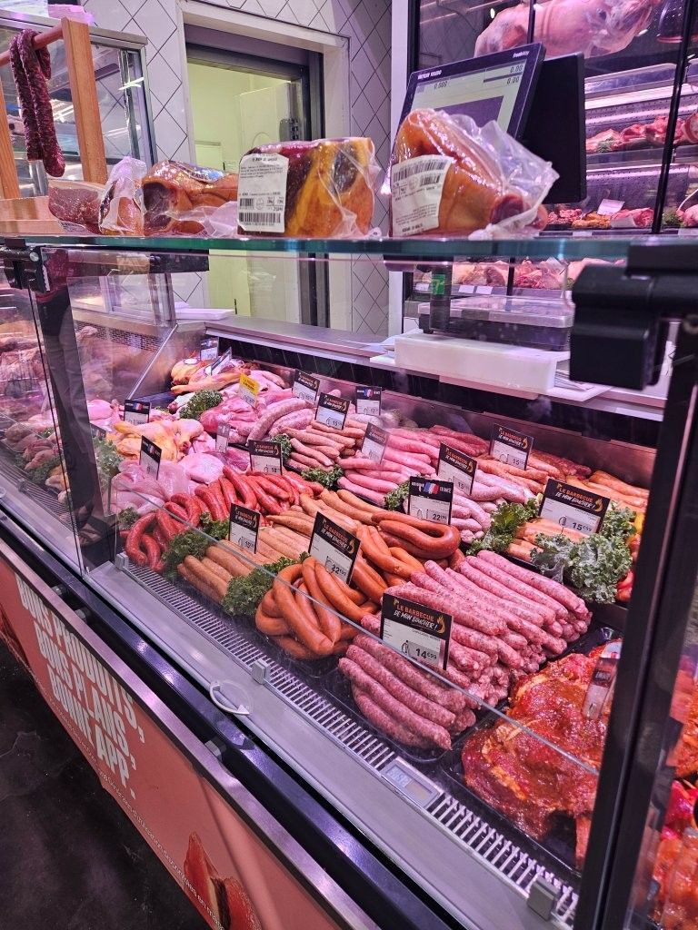 Die Auslage einer Metzgerei mit verschiedenen Fleischsorten und Wurstwaren, die in Reihen unter Glas präsentiert werden.