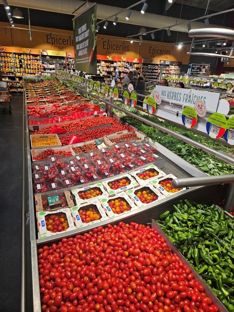 Obst- und Gemüseabteilung mit Erdbeeren, Tomaten und Paprika in einem Supermarktregal.