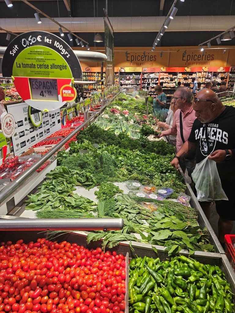 Gemüseauslage mit Tomaten, Blattgemüse und Paprika in einem belebten Lebensmittelmarkt.