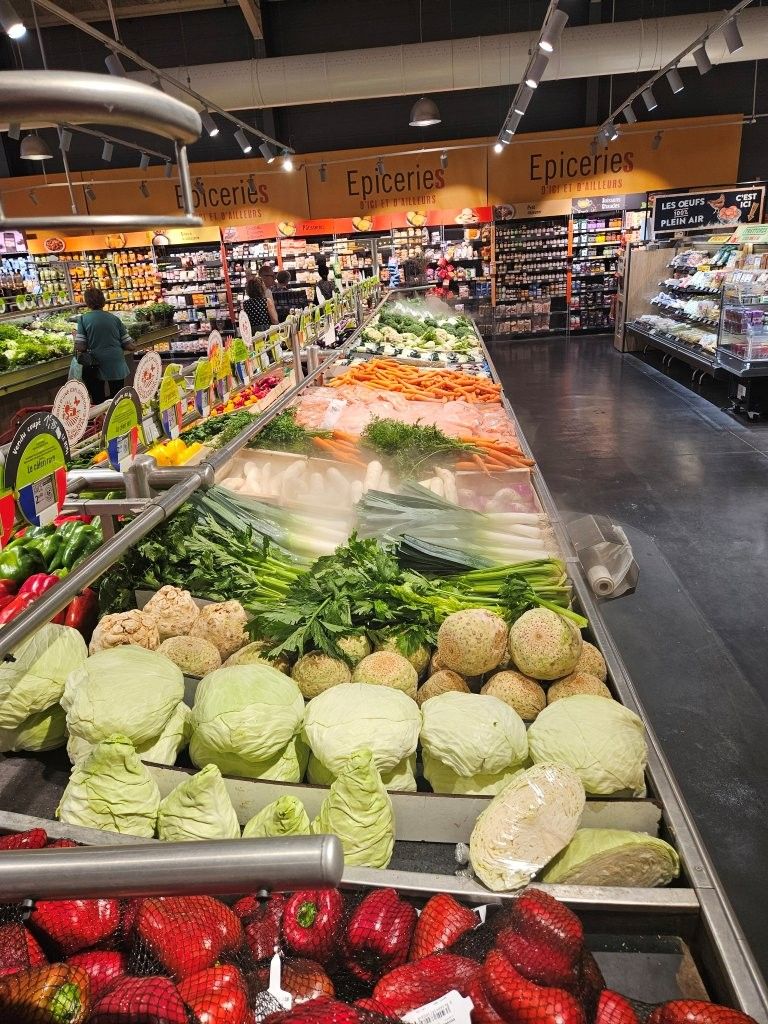 Die Obst- und Gemüseabteilung im Supermarkt mit Reihen von Kohl, Erdbeeren und anderem frischen Gemüse unter hellem Licht