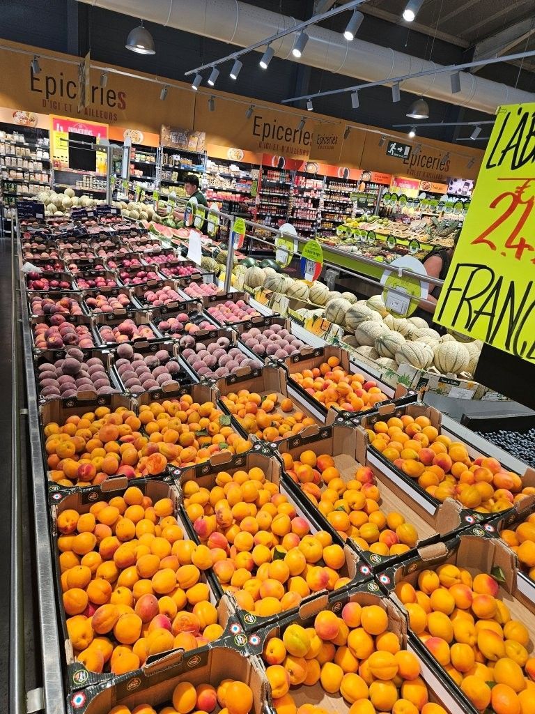 Obst- und Gemüseabteilung mit Kisten voller Orangen, Pfirsichen, Weintrauben und anderem Obst in einem Supermarkt.