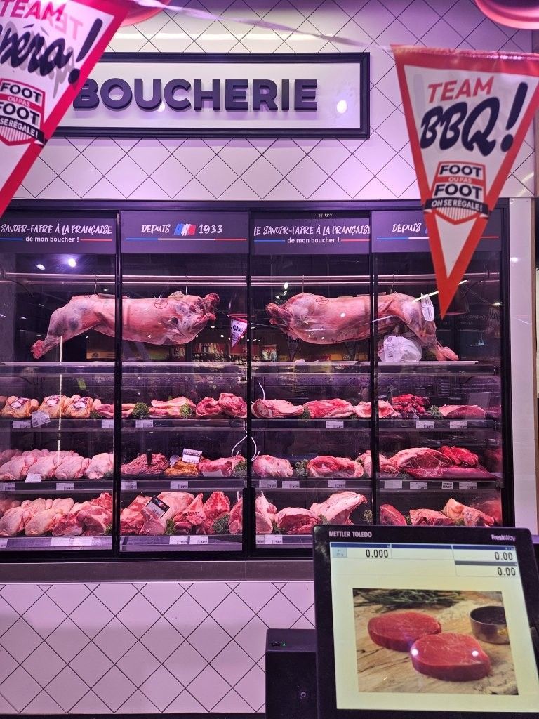 Auslage in einer Metzgerei mit Tabletts voller rohem Fleisch unter rosa Beleuchtung und einem kleinen Produktdisplay davor