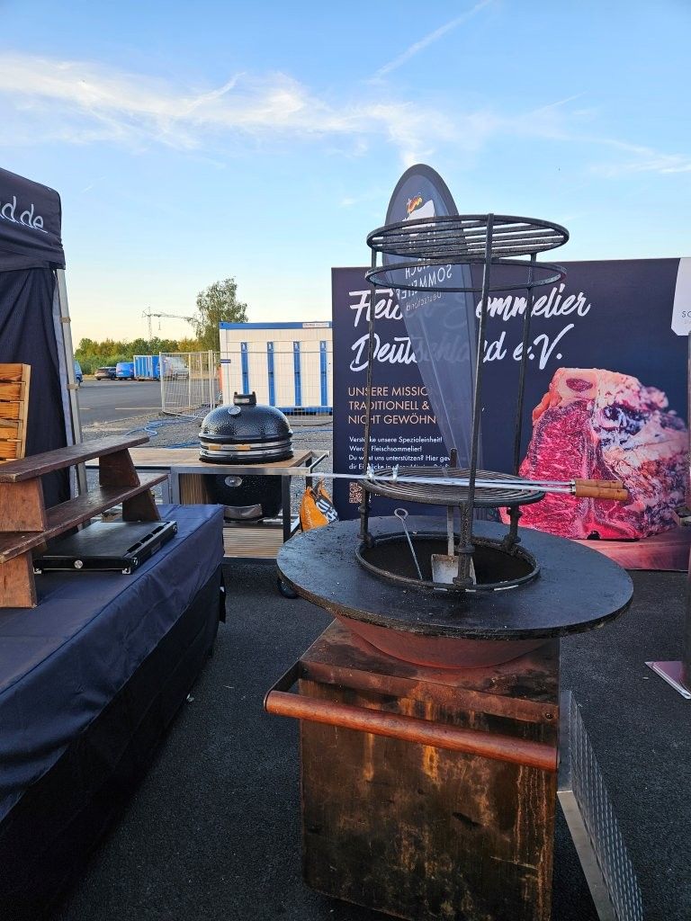 Marktstand im Freien mit rundem Grill, Kreidetafel-Menü und rosa Dessertschild bei Sonnenuntergang