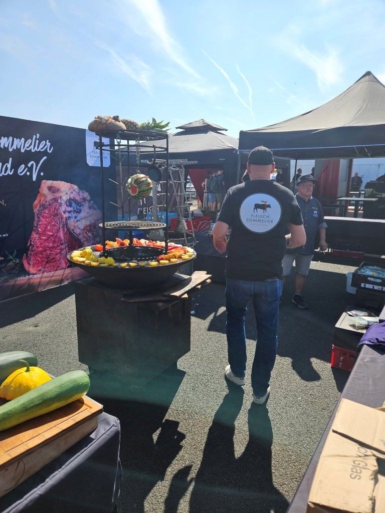 Marktstand im Freien mit einem runden Grill, Zelten und einer Person, die im Sonnenlicht steht