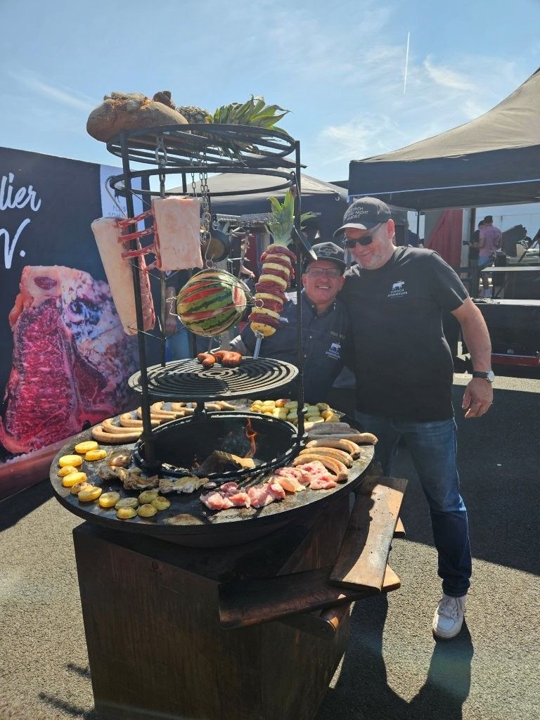 Menschen posieren neben einer großen Auslage mit Obst und Desserts an einem Marktstand im Freien.