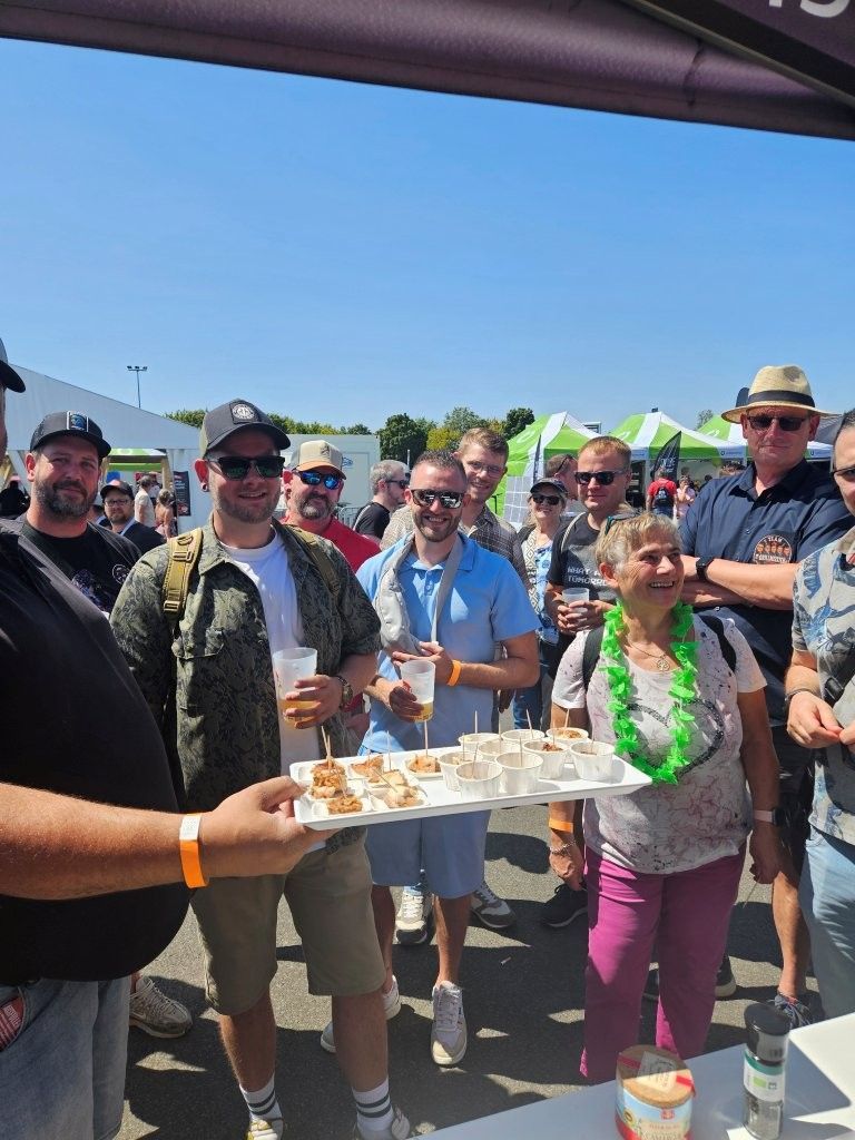 Eine Gruppe hatte sich bei sonnigem Wetter im Freien unter einem Baldachin versammelt und hielt ein Tablett mit Essen in den Händen. Alle lächelten.