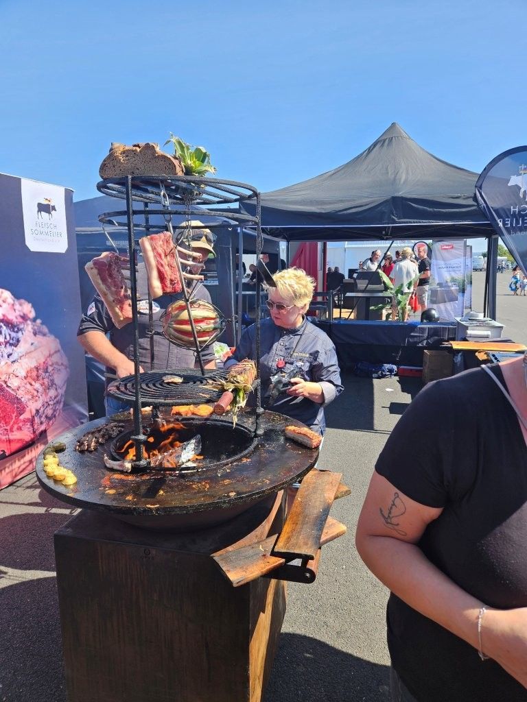 Marktstand im Freien mit einem vertikalen Drehspieß und einem Verkäufer, der unter schwarzen Zelten Speisen serviert.