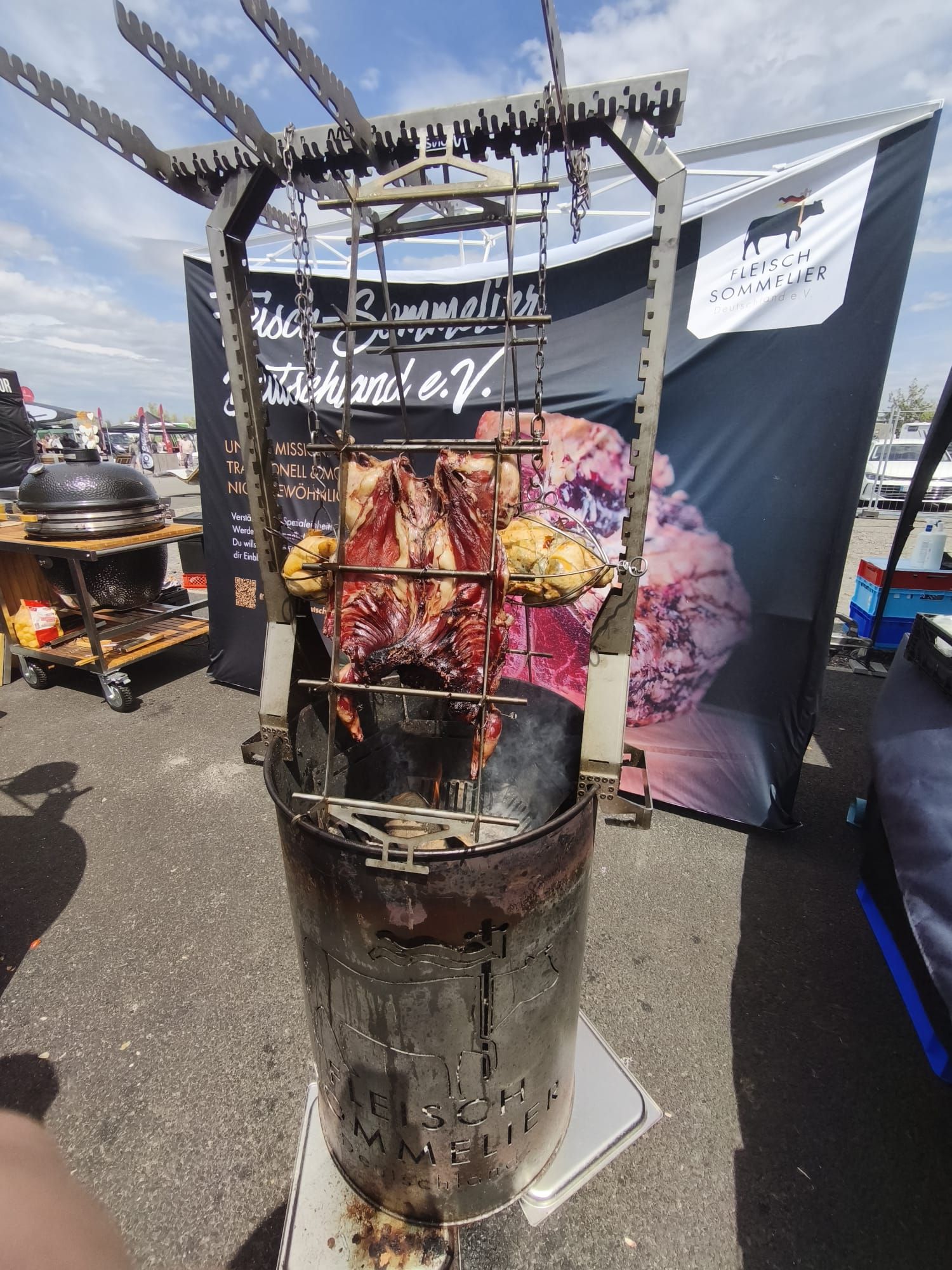 Imbissstand im Freien mit einem großen vertikalen Drehspieß, an dem Fleisch über Holzkohlerauch geröstet wird.