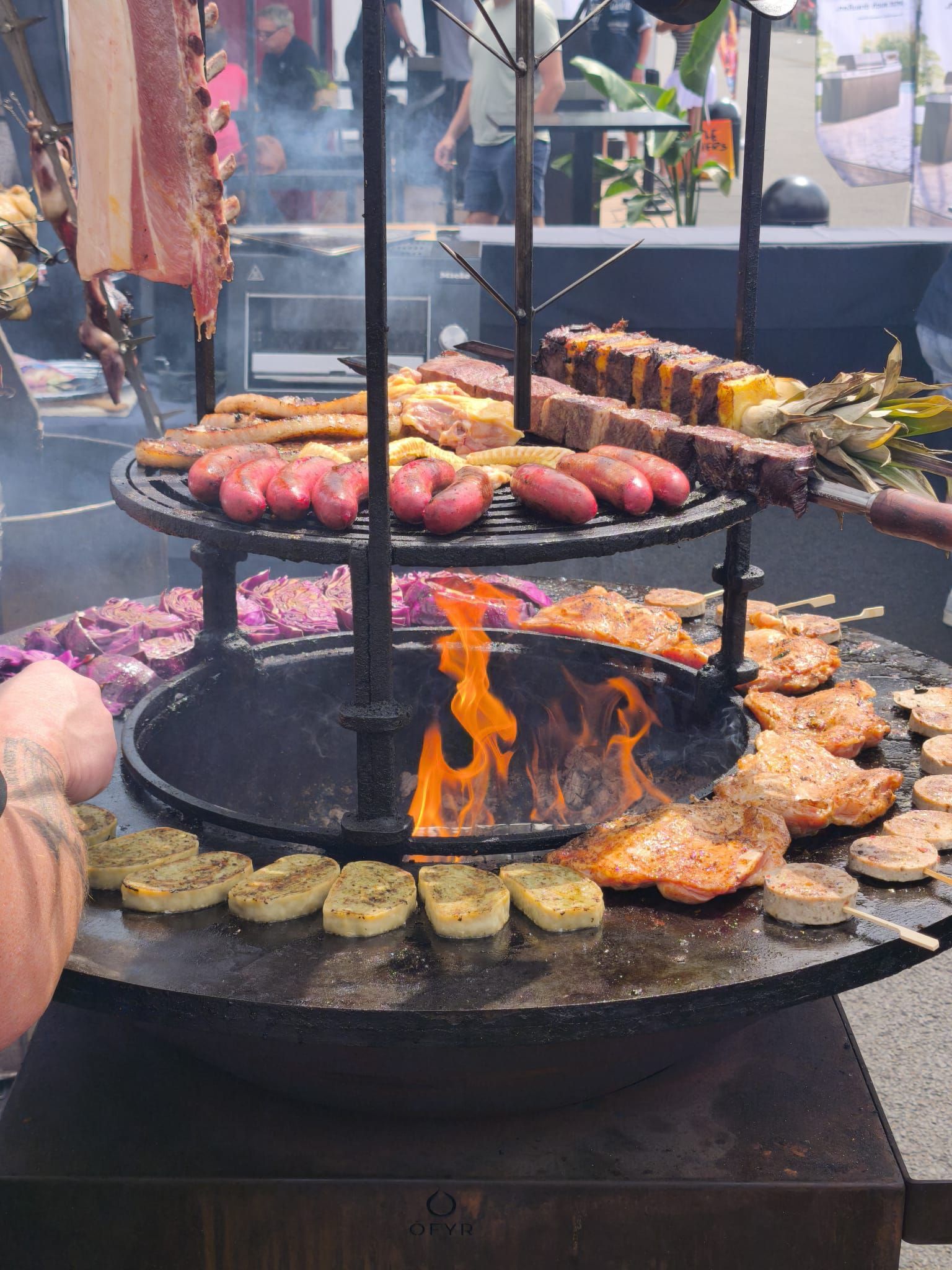 Grill im Freien mit verschiedenen Würstchen und Spießen, die über offener Flamme an einem Marktstand gegrillt werden.