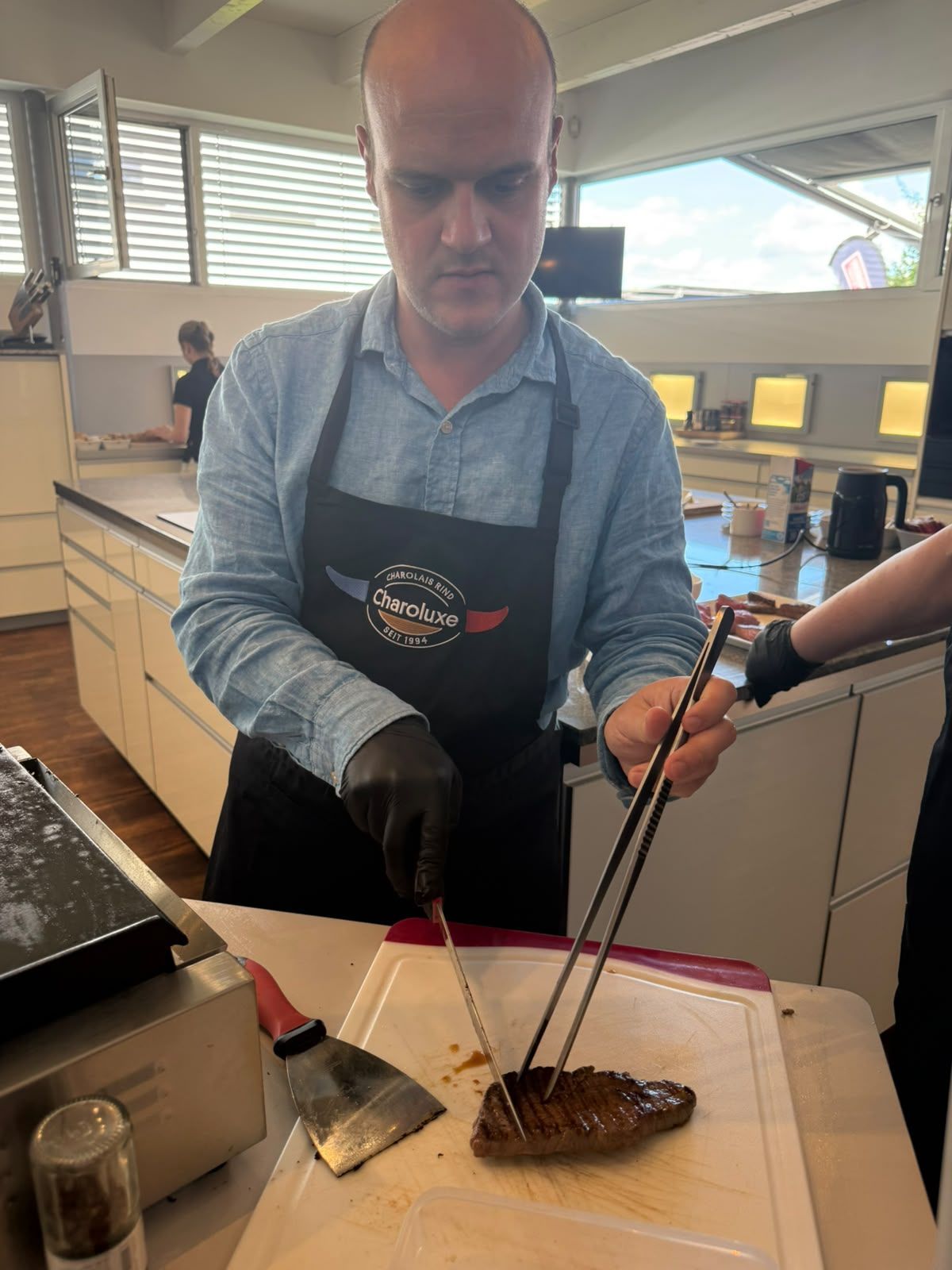 Ein Koch richtet in einer Küche ein gegrilltes Steak mit einer Zange und einem Pfannenwender an