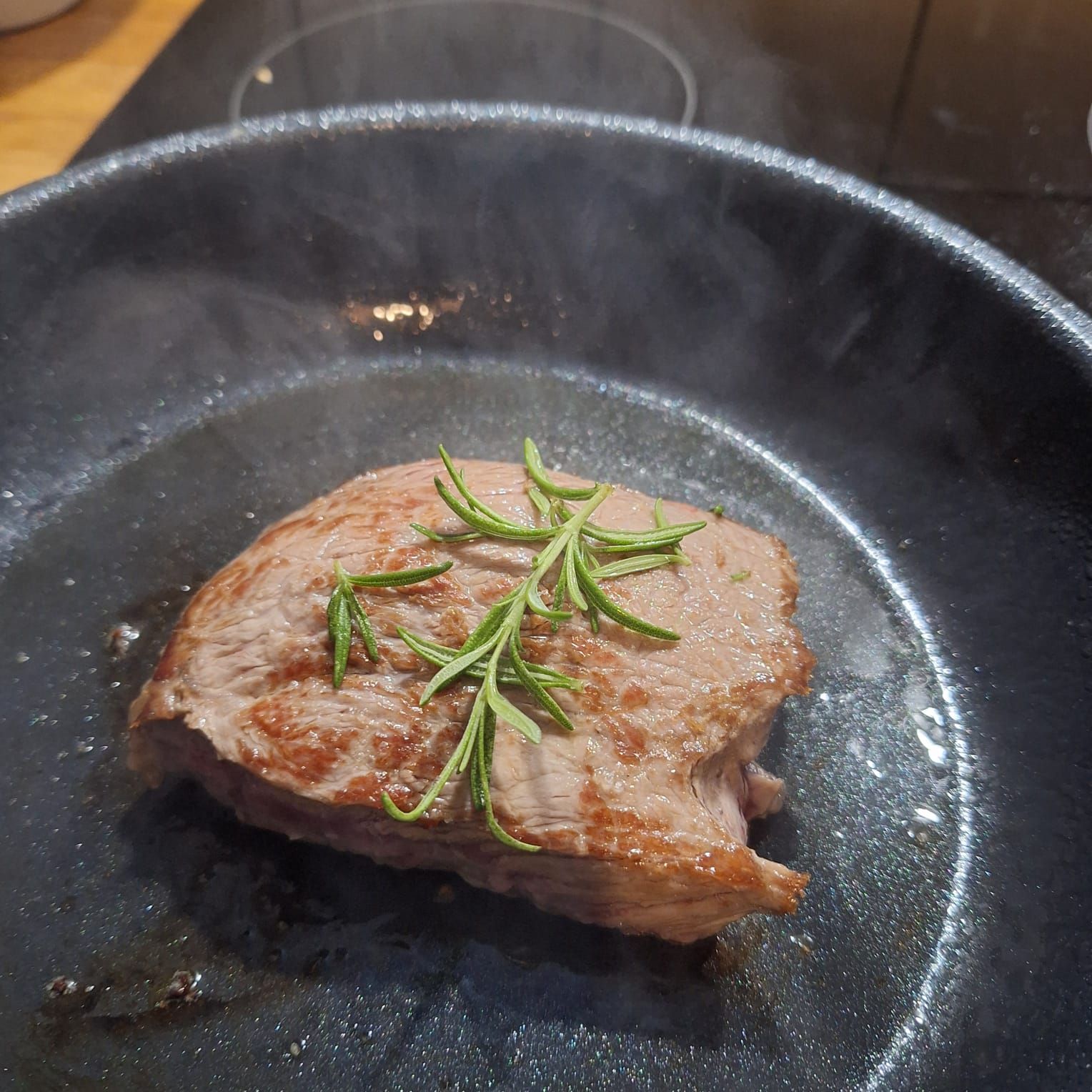 Dampfendes, scharf angebratenes Steak mit Rosmarin, in einer dunklen Pfanne