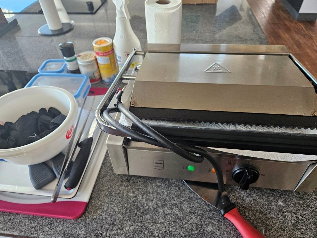 Sandwichmaker auf der Küchenarbeitsplatte neben einer Schüssel mit gehackten Zutaten und Würzmittel-Flaschen