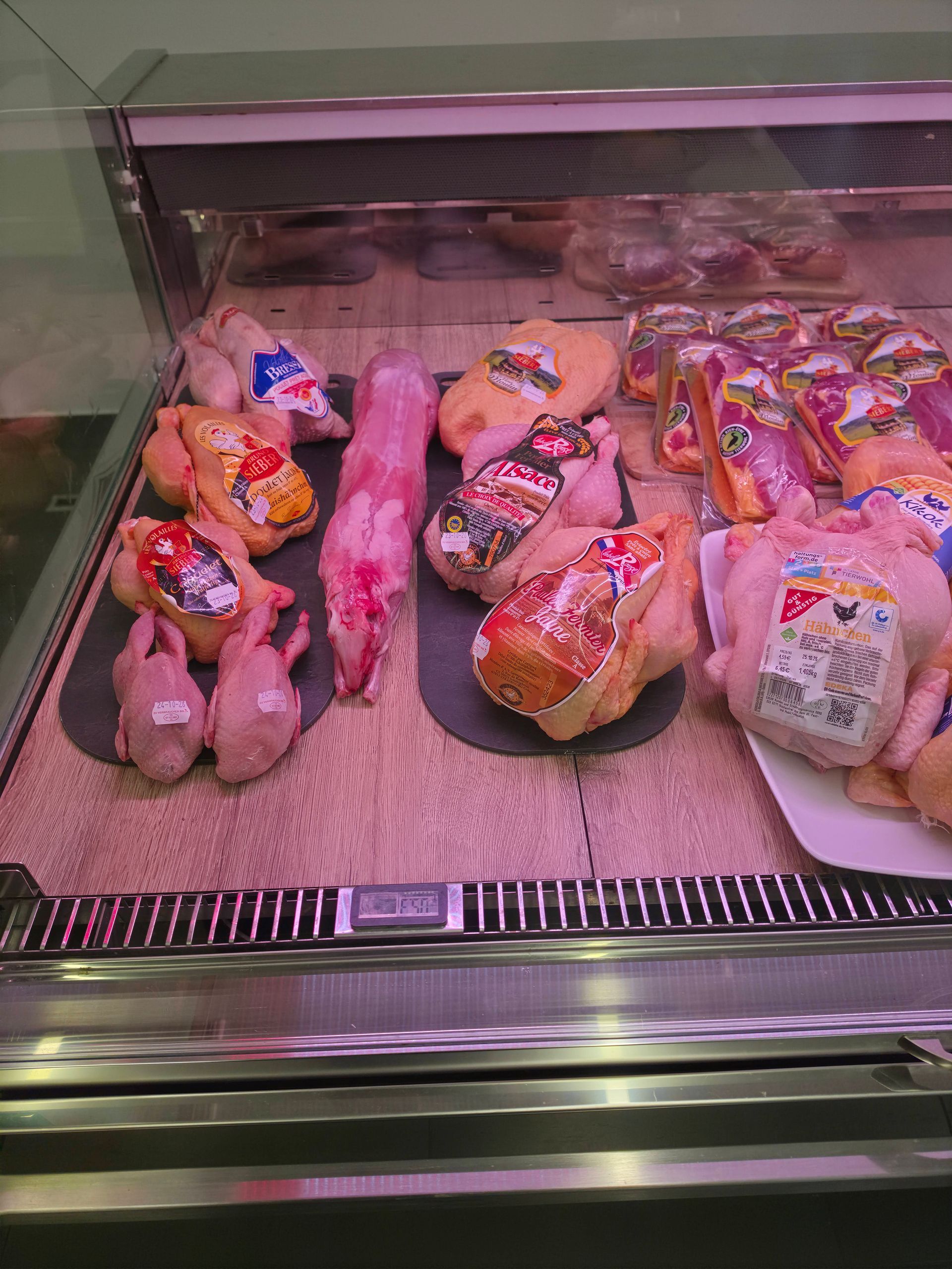Verschiedene abgepackte Wurstwaren in einer gekühlten Feinkosttheke mit rosa Beleuchtung