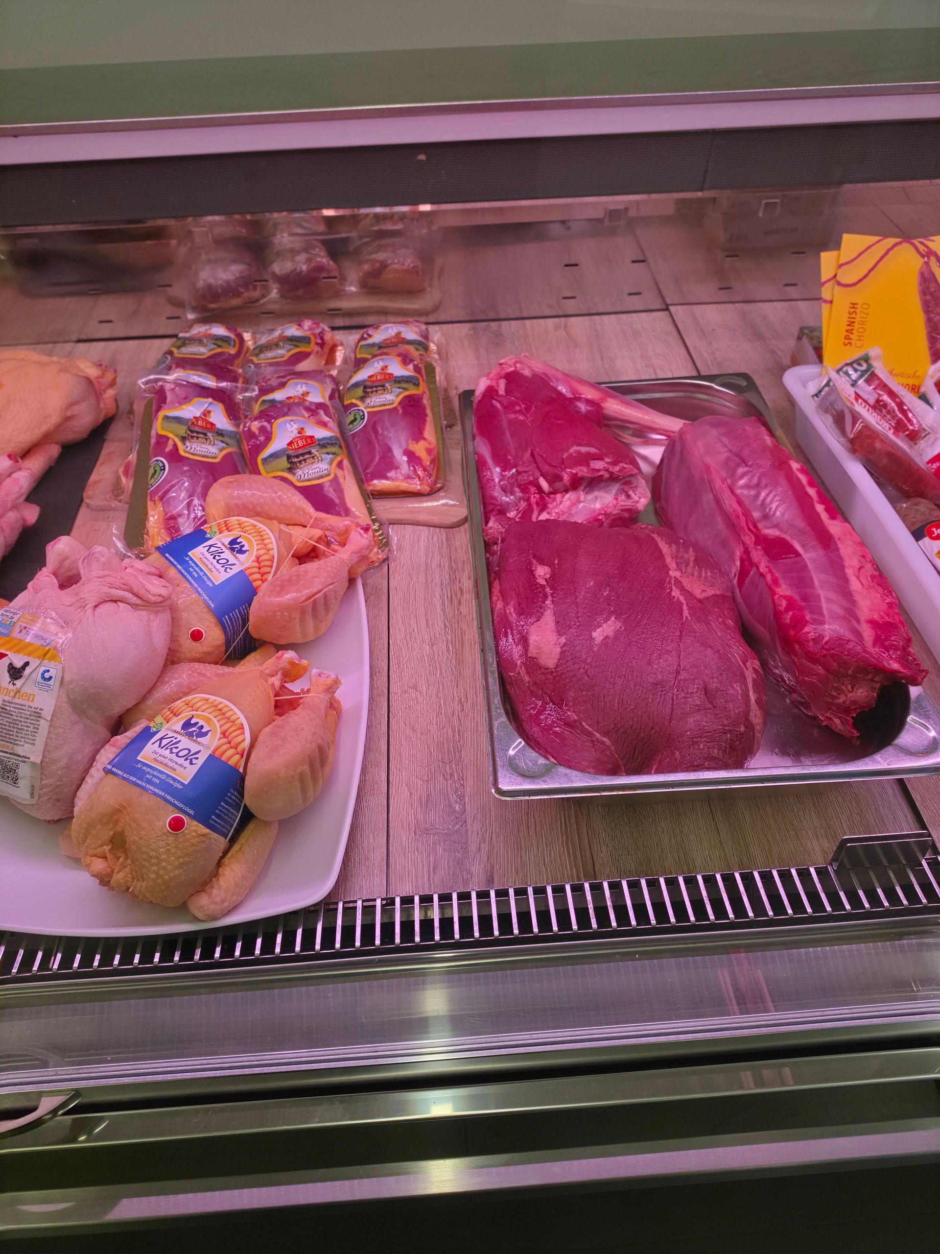 Kühltheke einer Metzgerei mit verpacktem Geflügel und rohem rotem Fleisch in den Auslagen